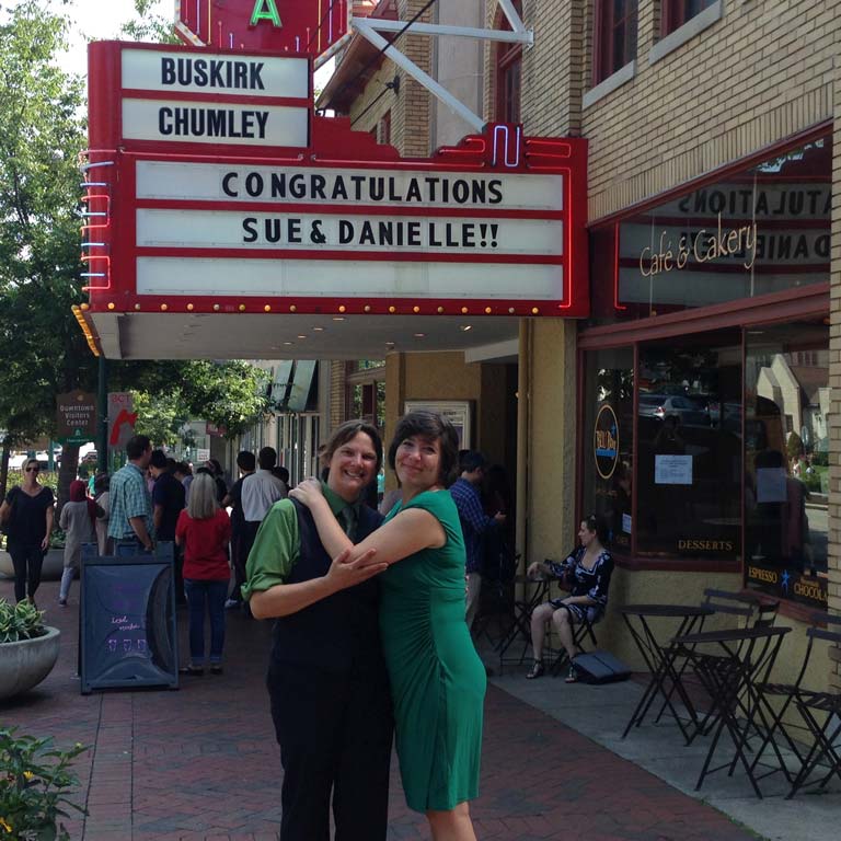 Two women embracing in front of a theatre marquee